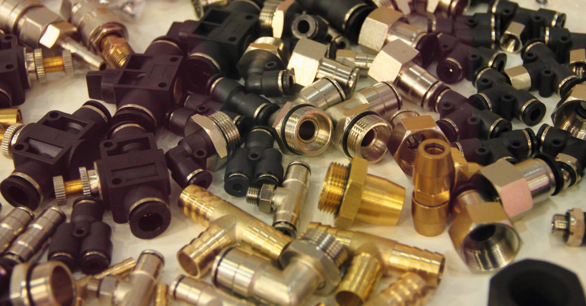 A variety of car fuel system fittings and connectors sit on a white surface. They feature various colors.