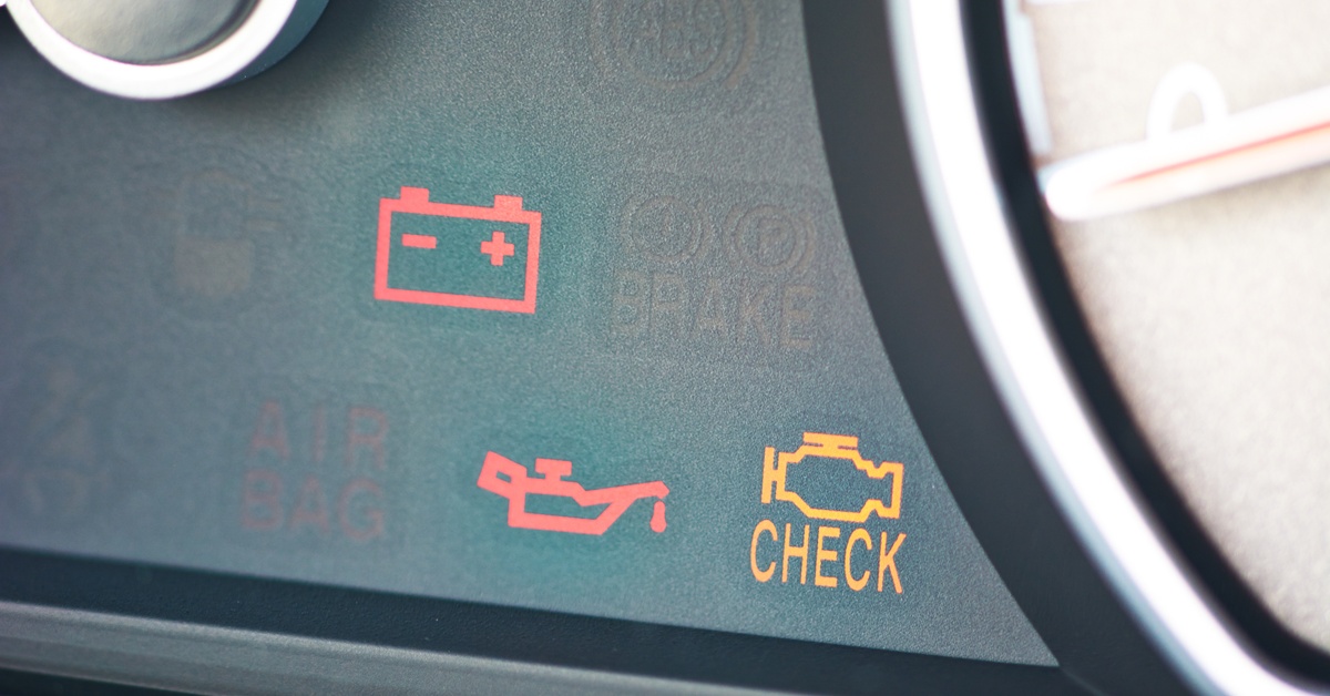 Close-up of a "check engine" light on a vehicle's dashboard. Other symbols appear, including one related to the battery.