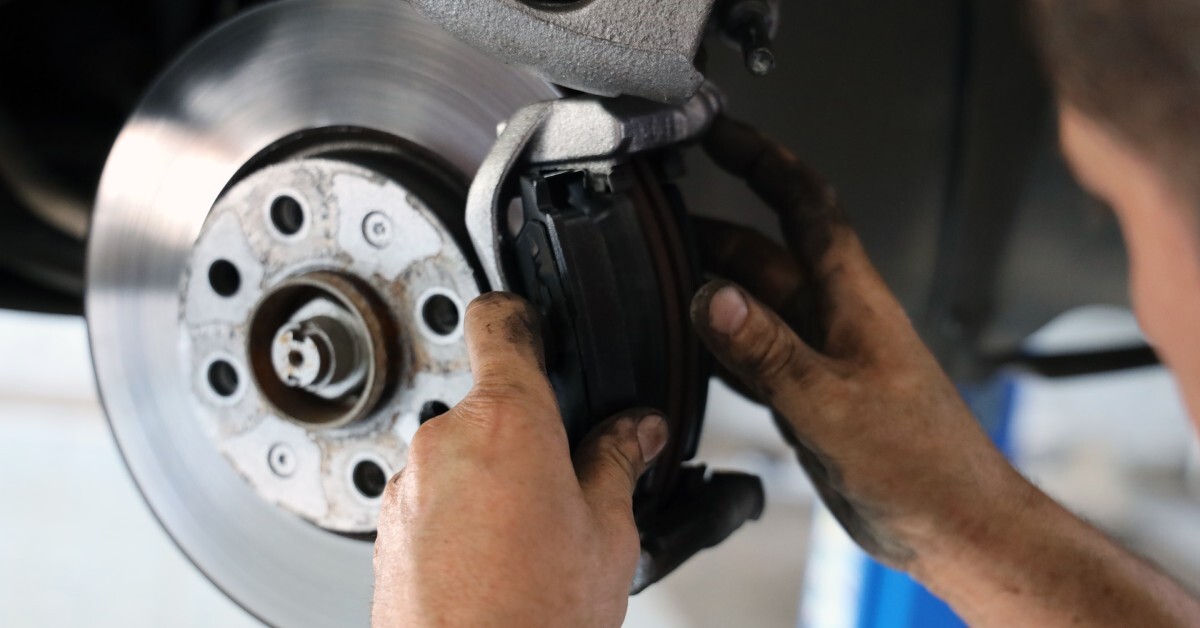 A man works on replacing the brake pads on his vehicle in an auto shop. The car is in the air on a lift.