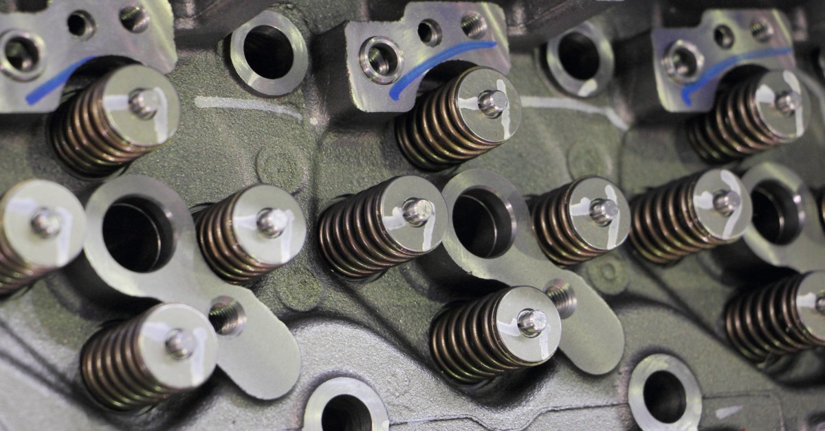 Close-up of a car's motor cylinder block head unit. It features various shiny valve springs and holes.