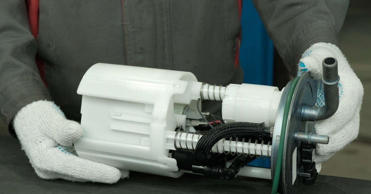 A mechanic's hand holds a new fuel pump for a car. The person handles it carefully while wearing white gloves.